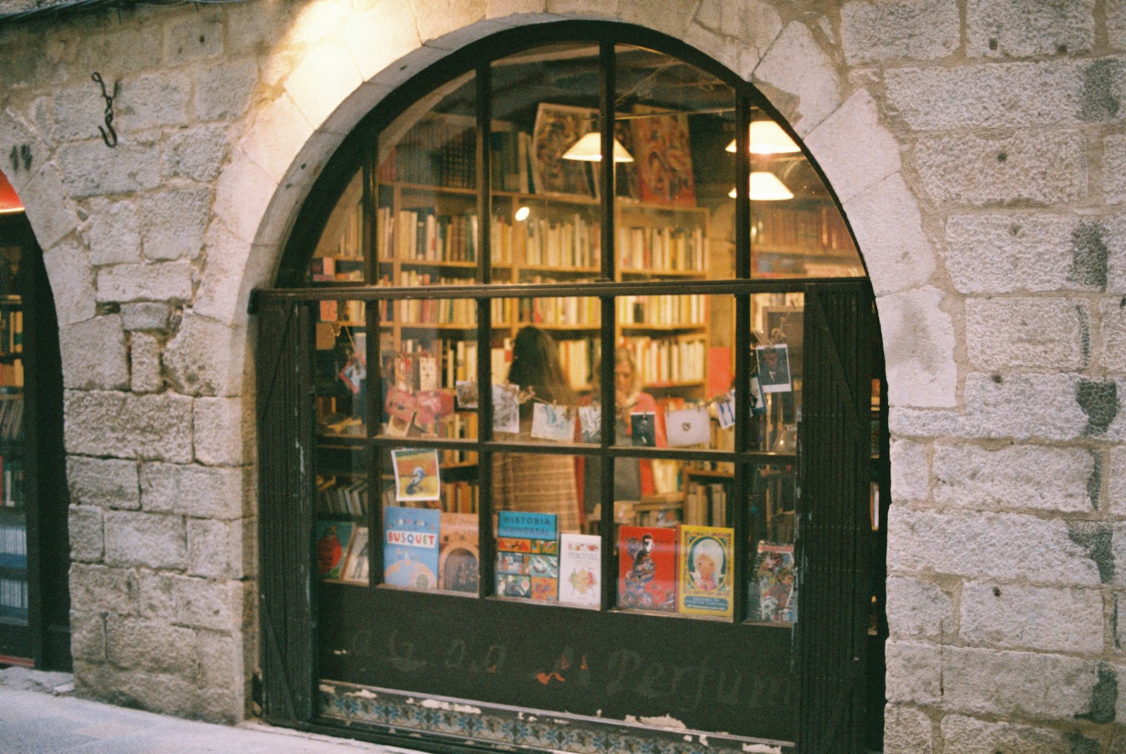 Arched stone shopfront window of a bookshop, books and postcards on display